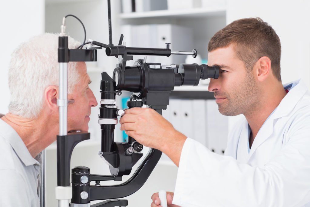 Male Optometrist Examining Senior Patients Eyes Through Slit Lam 